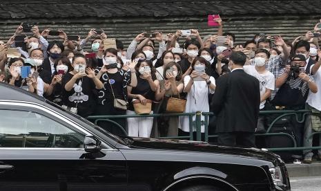 Orang-orang menyaksikan mobil jenazah yang membawa jenazah mantan Perdana Menteri Jepang Shinzo Abe saat meninggalkan kuil Zojoji setelah pemakamannya di Tokyo pada Selasa, 12 Juli 2022. Abe dibunuh Jumat saat berkampanye di Nara, Jepang barat.