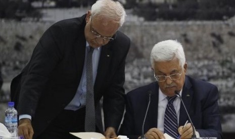 Palestinian chief negotiator Saeb Erekat (left) helps Palestinian President Mahmoud Abbas as he signs international conventions during a meeting with Palestinian leadership in the West Bank City of Ramallah April 1, 2014.