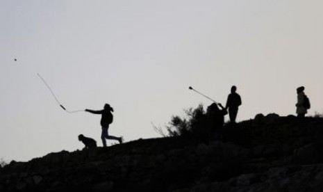 Palestinian protesters use slingshots to throw stones at Israeli troops during clashes near Israel's Ofer Prison, near the West Bank city of Ramallah December 13, 2014. 