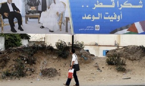 Palestinian youth walks near a poster of Gaza's Hamas Prime Minister Ismail Haniyeh (left) and Emir of Qatar Sheikh Hamad bin Khalifa al-Thani in Gaza City, Sunday, Oct. 21, 2012. The poster announces the coming visit of the Emir of Qatar, it reads, 