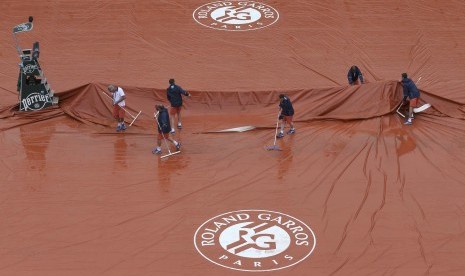 Para pekerja sedang membersihkan lapangan dari acara pembukaan turnamen Prancis Terbuka Roland Garros yang tergenang air