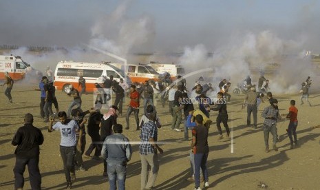  Para pengunjuk rasa Palestina berlindung dari gas air mata yang ditembakkan oleh pasukan Israel selama protes di perbatasan Jalur Gaza dengan Israel, sebelah timur Khan Younis, Jalur Gaza, pada Senin, 14 Mei 2018. Ribuan warga Palestina melakukan protes di dekat perbatasan Gaza dengan Israel saat Israel sedang mempersiapkan perayaan meriah Kedutaan Besar AS di Yerusalem.