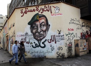 Pasangan warga Mesir berjalan melintasi sebuah gambar wajah penguasa militer Marsekal Hussein Tantawi dan mantan Presiden Hosni Mubarak di Tahrir Square, Kairo, Mesir. 