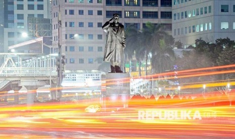 Patung Jenderal Sudirman di timpali Lintasan sinar lampu mobil berpadu dengan lansekap kota malam hari di Jl Jendral Sudirman, Jakarta.