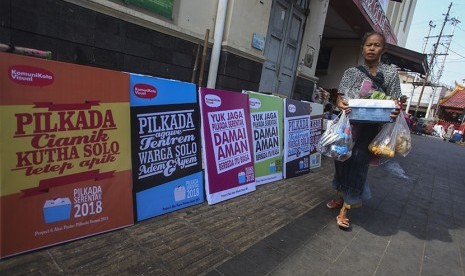 Pedagang melewati jajaran poster Pilkada Damai 2018 yang dipajang di kawasan Pasar Gede, Solo, Jawa Tengah, Senin (25/6). 