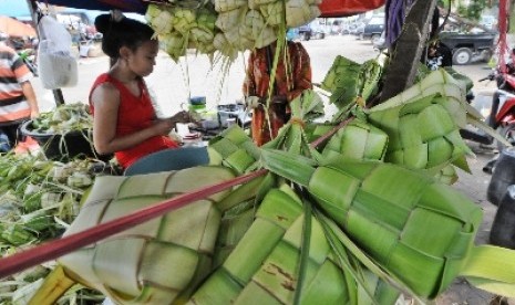 Pedagang merangkai janur kelapa menjadi ketupat.