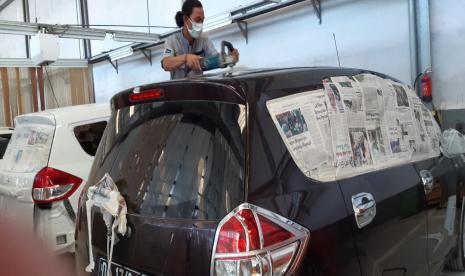 Pegawai bengkel sedang memoles dan membersihkan mobil pelanggan