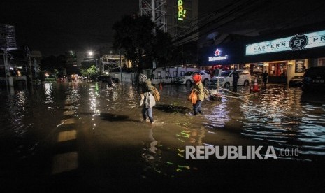 Pejalan berusaha melintasi banjir yang menggenangi kawasan niaga Kemang, Ahad malam (25/9).