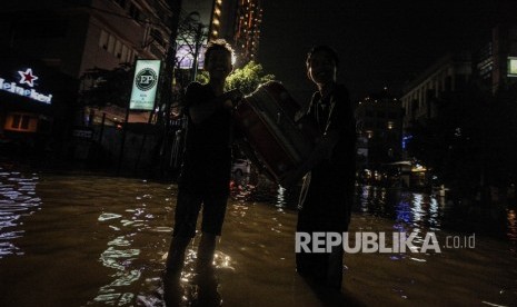 Pejalan berusaha melintasi banjir yang menggenangi kawasan niaga Kemang, Ahad malam (25/9).