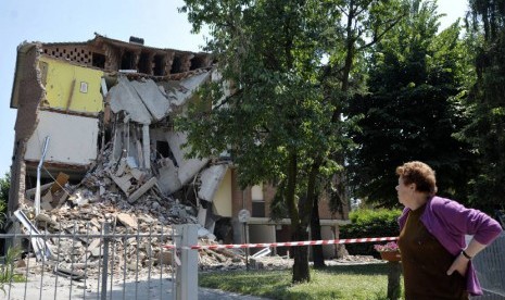  Pejalan kaki melewati bangunan yang runtuh akibat gempa bumi di Cavazzo, Italia, Selasa (29/5). (Marco Vasini/AP)