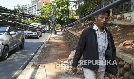 Pejalan kaki melintas di dekat kabel yang terjuntai semrawut di trotoar di Jalan Kemang Raya, Jakarta, Selasa (22/10/2019). 