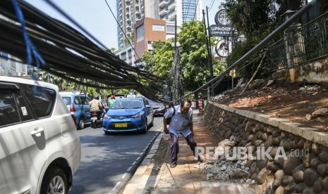 Pejalan kaki melintas di dekat kabel yang terjuntai semrawut di trotoar di Jalan Kemang Raya, Jakarta, Selasa (22/10/2019). 