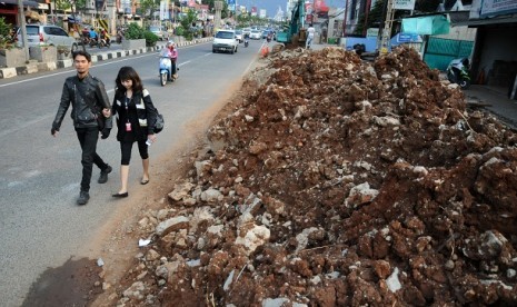 Pejalan kaki melintas di samping tanah galian proyek pembuatan drainase yang belum diangkut di badan jalan Margonda Raya, Depok, Jawa Barat, Selasa (10/12). 