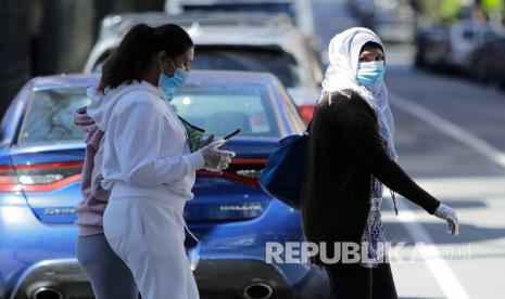 Pejalan kaki mengenakan masker dan sarung tangan melintasi Roosevelt Avenue, New York, Sabtu (4/4). Karyawan rumah sakit curi APD di tengah kelangkaan persediaan di AS. Ilustrasi.