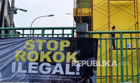 Pekerja beraktivitas di dekat spanduk kampanye stop rokok ilegal, ilustrasi. Kantor Pengawasan dan Pelayanan Bea Cukai Tipe Madya Cukai Malang menggagalkan pengiriman rokok ilegal yang menggunakan jasa ekspedisi dari wilayah Malang Raya, Jawa Timur.