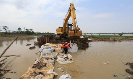 Pekerja dari Balai Besar Wilayah Sungai Cimanuk-Cisanggarung (BBWS) menggunakan alat berat memperbaiki tanggul sungai Cipanas yang kembali jebol di desa Puntang, Losarang, Indramayu, Jawa Barat, Ahad (28/2/2021). Tanggul Sungai Cipanas kembali jebol akibat tingginya debit air hingga menyebabkan banjir merendam empat desa di kecamatan Losarang. 