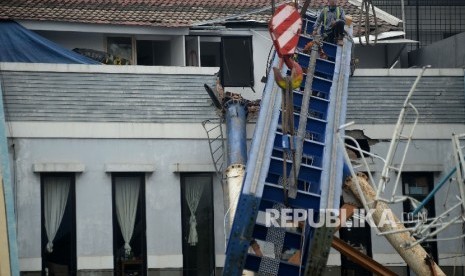 Pekerja dengan menggunakan alat berat melakukan evakuasi tiang proyek konstruksi Light Rail Transit (LRT) yang menimpa rumah warga di Kawasan Kelapa Gading, Jakarta, Selasa (17/10).