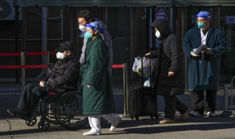 Pekerja medis dengan alat pelindung mengawal seorang pasien lanjut usia di kursi roda diikuti oleh anggota keluarga saat mereka meninggalkan klinik demam di sebuah rumah sakit di Beijing pada Senin, 19 Desember 2022. Jerman telah mengirimkan sejumlah vaksin Covid-19 BioNTech-Pfizer ke China.