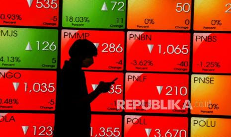 Pekerja melihat telepon pintarnya dengan latar belakang layar pergerakan harga saham di Bursa Efek Indonesia, Jakarta, Rabu (31/3). IHSG dibuka melemah 0,45 poin atau 0,01 persen ke posisi 6.060,31. 