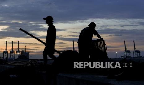 Pekerja membuang kulit kerang hijau dengan latar belakang aktivitas bongkar muat barang di Cilincing, Jakarta, Jumat (31/12/2021). Pemerintah optimis pertumbuhan ekonomi 2022 membaik ditandai dengan pelaksanaan APBN 2021 sesuai perencanaan serta kinerja pendapatan dan belanja negara yang positif mengindikasikan pemulihan ekonomi terus berlanjut.