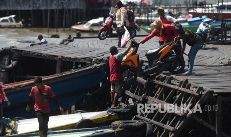 Pekerja menaikkan motor ke atas perahu cepatnya di Pelabuhan Penyebrangan Penajam Paser Utara, Kalimantan Timur.