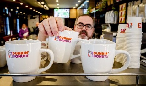 Pekerja menata cangkir minum di gerai Dunkin Donuts.