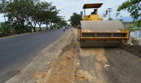 Pekerja mengoperasikan alat berat pada proyek pelebaran jalan. 