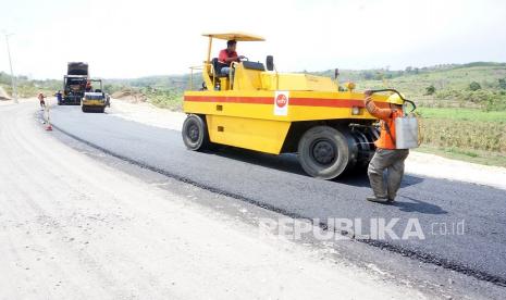 Pekerja mengoperasikan alat berat untuk memadatkan aspal hotmix jalur lintas selatan (JLS) yang sedang dibangun di pesisir selatan Pucanglaban, Tulungagung, Jawa Timur, Ahad (26/9/2021). Dari total rencana JLS sepanjang 52 kilometer yang melintasi kawasan pesisir selatan Tulungagung, hingga akhir Agustus yang telah selesai dibangun sekitar 22 kilometer dan diharapkan rampung pada 2024. 