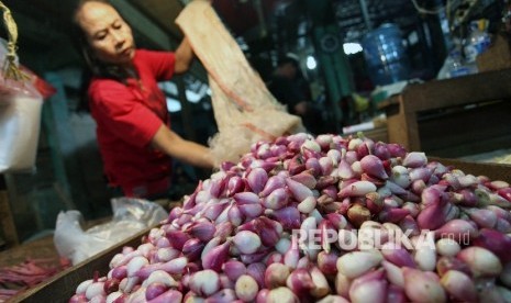 Pekerja mengupas bawang merah di pasar.