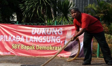 Pekerja sedang membawa selang berlatar belakang spanduk dukungan Pilkada langsung di kawasan Menteng, Jakarta, Senin (22/9).(Republika/ Tahta Aidilla)