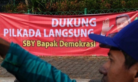 Pekerja sedang membawa selang berlatar belakang spanduk dukungan Pilkada langsung di kawasan Menteng, Jakarta, Senin (22/9).(Republika/ Tahta Aidilla)