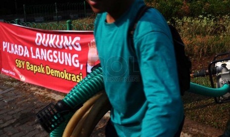 Pekerja sedang membawa selang berlatar belakang spanduk dukungan Pilkada langsung di kawasan Menteng, Jakarta, Senin (22/9).(Republika/ Tahta Aidilla)