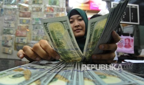 Pekerja sedang menghitung mata uang dolar di money changer.