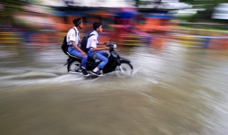 Pelajar menerobos genangan banjir.