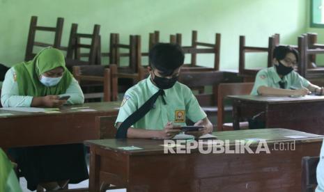 Pelajar mengerjakan soal Ujian Satuan Pendidikan (USP) mata pelajaran Pendidikan Pancasila dan Kewarganegaraan menggunakan gawai di SMP Negeri 1 Ngasem, Kediri, Jawa Timur, Kamis (25/3/2021). Sejumlah sekolah di daerah tersebut mewajibkan siswa hadir di sekolah dengan menerapkan protokol kesehatan COVID-19 meskipun USP diselenggarakan secara daring guna mempermudah pemantauan.