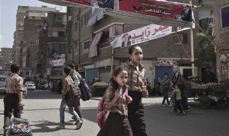 Pelajar Mesir pulang sekolah melewati sebuah spanduk yang memuat foto kandidat anggota parlemen dalam berbahasa Arab di jalan Boulaq El Dakrour di distrik Giza, dekat Kairo, Mesir, Kamis (8/10).