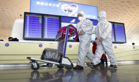 Pelancong mengenakan masker dan pakaian perlindungan untuk menjaga penyebaran virus corona jenis baru melewati papan pengumuman di Bandara Wuhan Tianhe, di Wuhan, Hubei, Rabu (8/4). Kebijakan lockdown mulai diangkat mengakibatkan ribuan orang meninggalkan kota dengan pesawat dan kereta. 