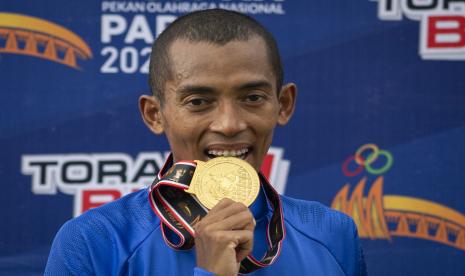 Pelari Jawa Barat Agus Prayogo berpose menggigit medali usai menjuarai final nomor lari 5.000 meter putra cabang atletik PON Papua di Stadion Atletik Mimika Sport Center, Kabupaten Mimika, Papua, Selasa (5/10/2021). Agus meraih medali emas, sementara pelari Jabar lainnya Pandu Sukarya meraih medali perak dan pelari Bangka Belitung Robi Sianturi meraih medali perunggu. 