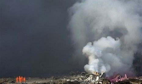 Pemadam kebakaran dengan pakaian pelindung berdiri di samping asap yang membumbung dari sebuah gudang di Tianjin, Cina, Kamis (13/8). 