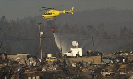 Pemadam kebakaran menggunakkan helikopter untuk menyiramkan air di puing bekas kebakaran.