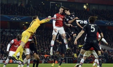 Pemain Arsenal, kiper Wojciech Szczesny (kiri) dan Laurent Koscielny (tengah), terlibat duel udara dengan pemain Bayern Muenchen, Javi Martinez, di leg pertama babak 16 besar Liga Champions.  