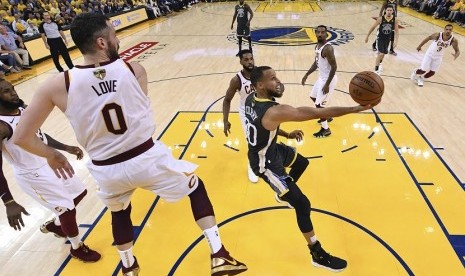 Pemain Guard Golden State Warrios, Stephen Curry (kanan) melakukan lay up di tengah adangan forward Cleveland Cavaliers, Kevin Love di gim kedua final NBA. Di pertandingan ini Warrios menang 122-103. 