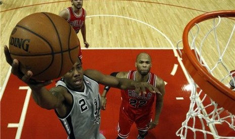 Pemain San Antonio Spurs, Kawhi Leonard (kiri), 'terbang' menjaringkan bola melawan pemain Chicago Bulls, Joakim Noah (tengah) dan Taj Gibson, di kompetisi NBA di Chicago pada Senin (11/2). 