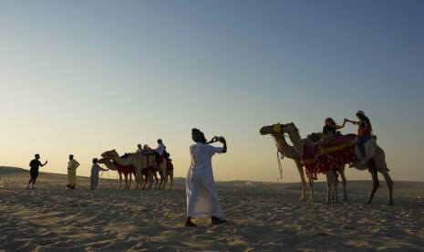 Pemandu wisata mengambil foto pasangan di atas unta di Mesaieed, Qatar, 26 November 2022. 