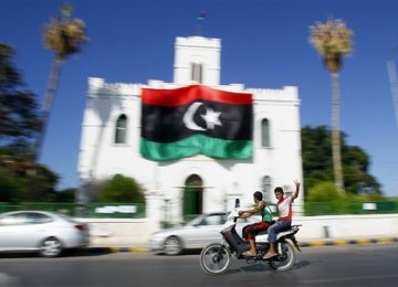 Pemuda Libya mengacungkan jari tangan tanda kemenangan ketika melintas di depan gedung Al-Ajaylat yang kini dikuasai pemberontak, sekitar 120 kilometer barat Tripoli, Libya.