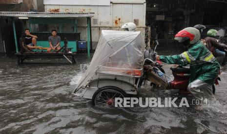 Pengemudi mendorong becak motornya yang mogok saat menerobos banjir di Jalan Petemon Timur, Surabaya.