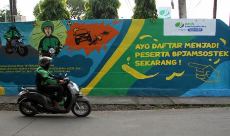 Pengemudi ojek daring melintas di depan mural sosialisasi pentingnya menjadi peserta BPJS Ketenagakerjaan (BPJAMSOSTEK). 