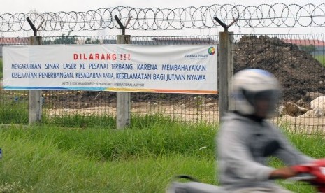 Pengendara bermotor melintas di dekat sepanduk bertuliskan larangan mengarahkan sinar laser ke pesawat 