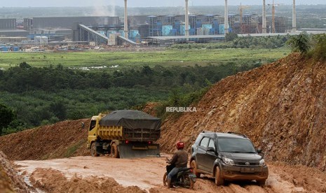 Pengendara berusaha melintasi jalan Trans Sulawesi yang rusak dan berlumpur dengan latar belakang pabrik smelter di Kecamatan Morosi, Konawe, Sulawesi Tenggara, Selasa (22/5). 