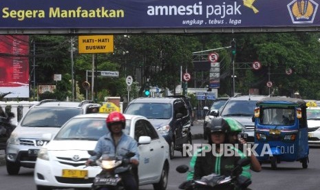  Pengendara melintas di dekat spanduk sosialisai pengampunan pajak yang terpasang di jembatan Penyebrangan orang (JPO) di kawasan Stasiun Gambir, Jakara, Ahad (31/7).  (Republika/ Agung Supriyanto)